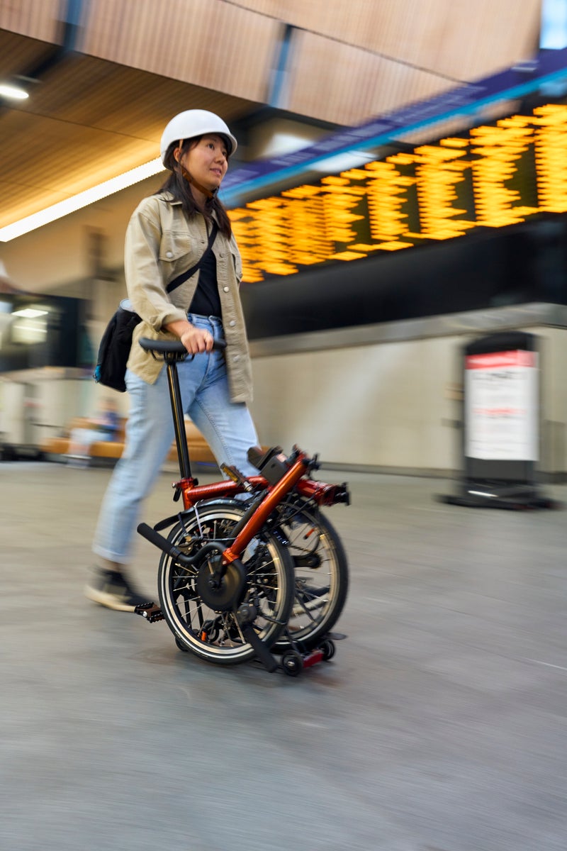 person wheeling a folded brompton bike through train station in London