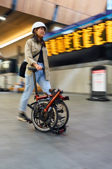 a woman wheeling a folded brompton electric p line through train station
