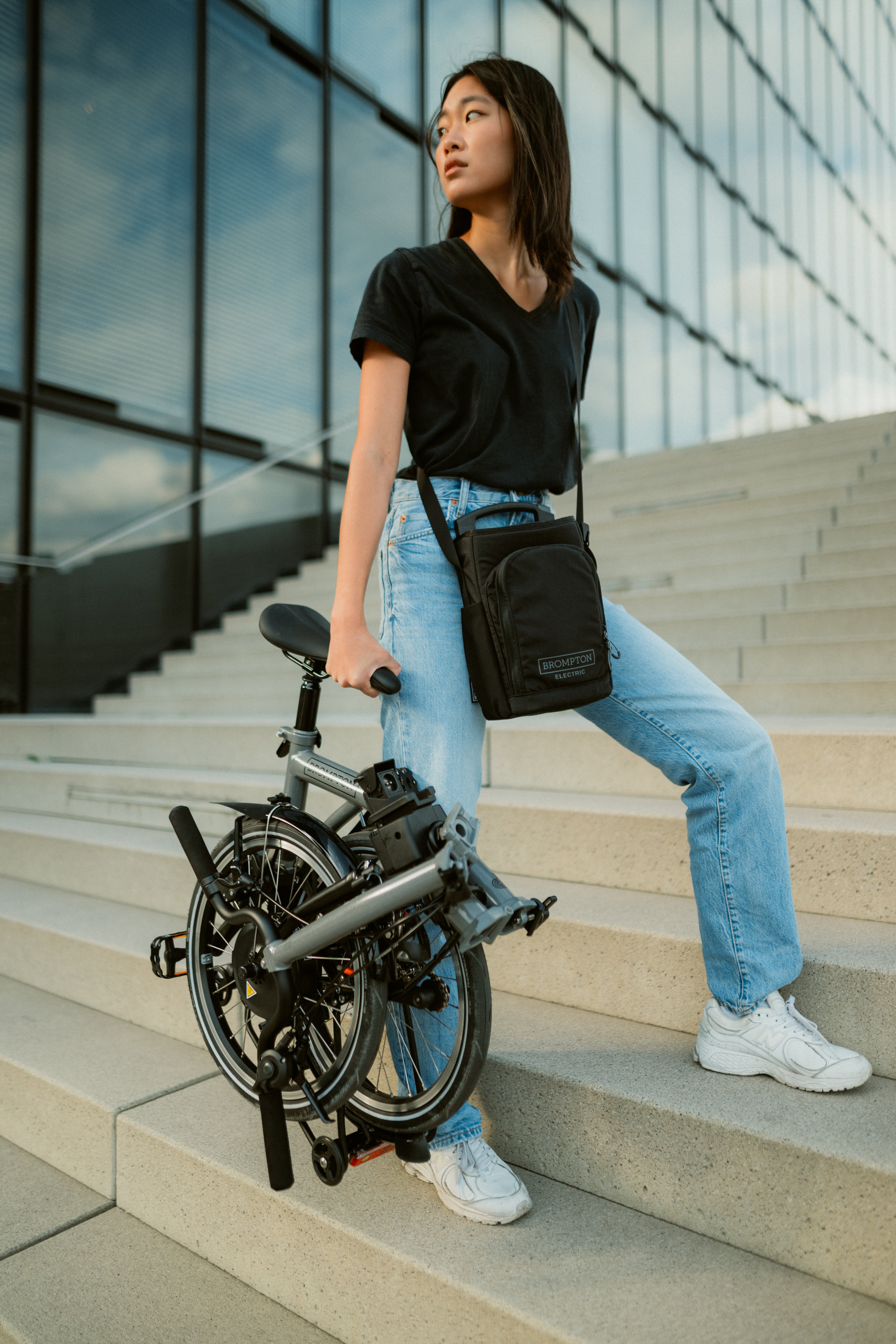 A woman carrying a folded Brompton Electric P Line up a set of stairs