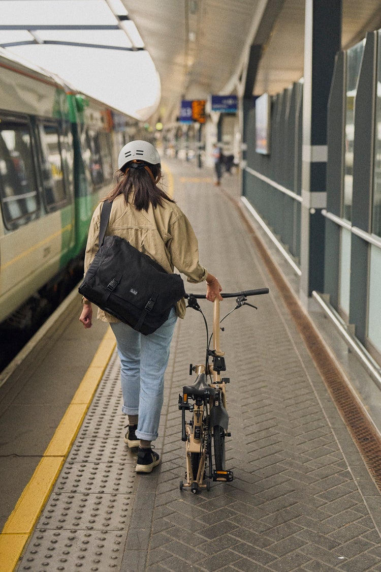 woman rolling a folded brompton c line in dune sand on train platform