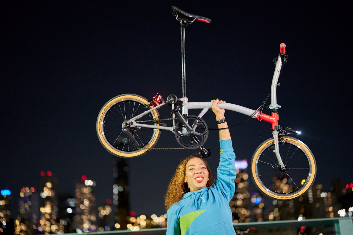 A woman triumphantly raising a Brompton CHPT3 over her head in NYC at night