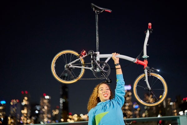Una mujer sostiene triunfante una bicicleta Brompton CHPT3 sobre su cabeza