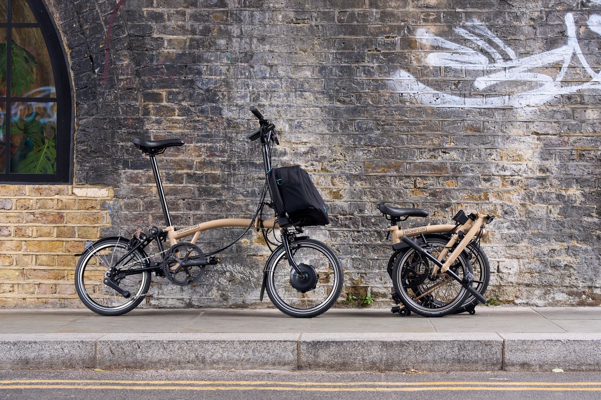 Brompton Electric C Line in Dune Sand leaning against brick wall