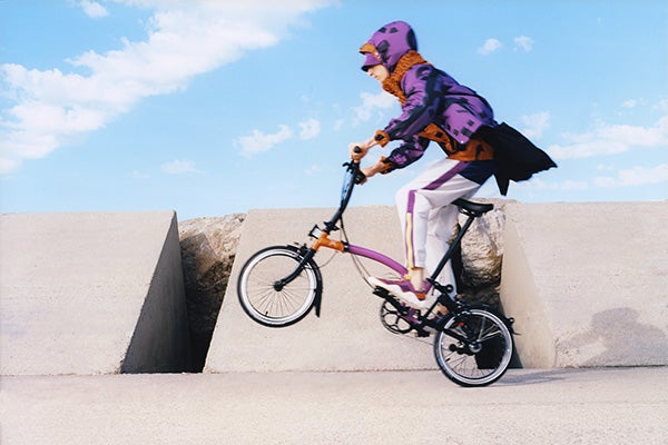 Persona montando una bicicleta Kenzo x Brompton con chaqueta morada.