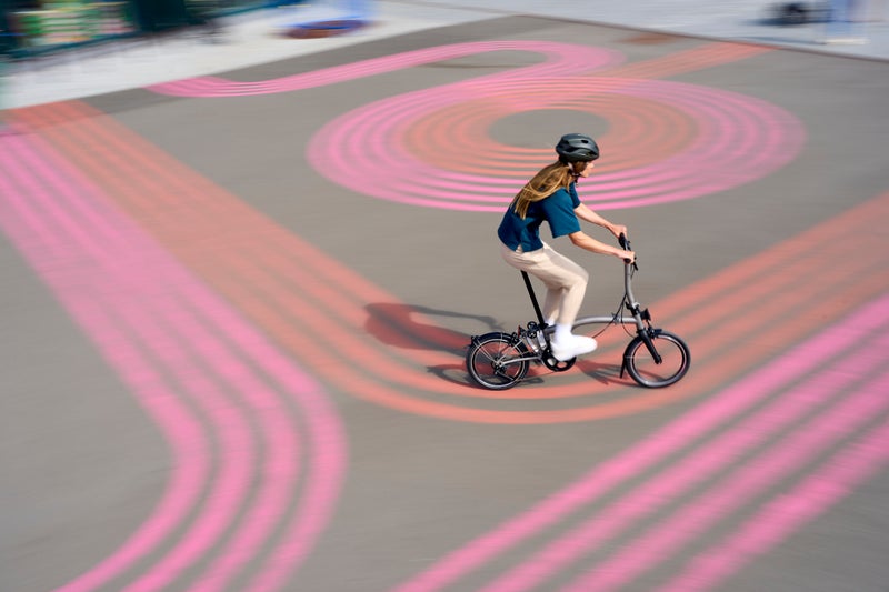 donna in bicicletta brompton in campo rosa