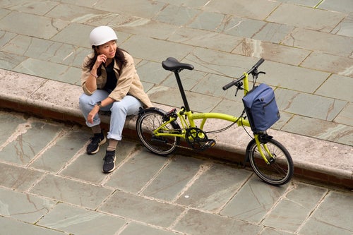 person sat on pavement in white helmet with brompton c line yuzu lime 