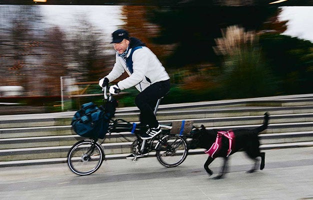 Man rijdt op een Brompton-fiets met een zwarte hond die meerent