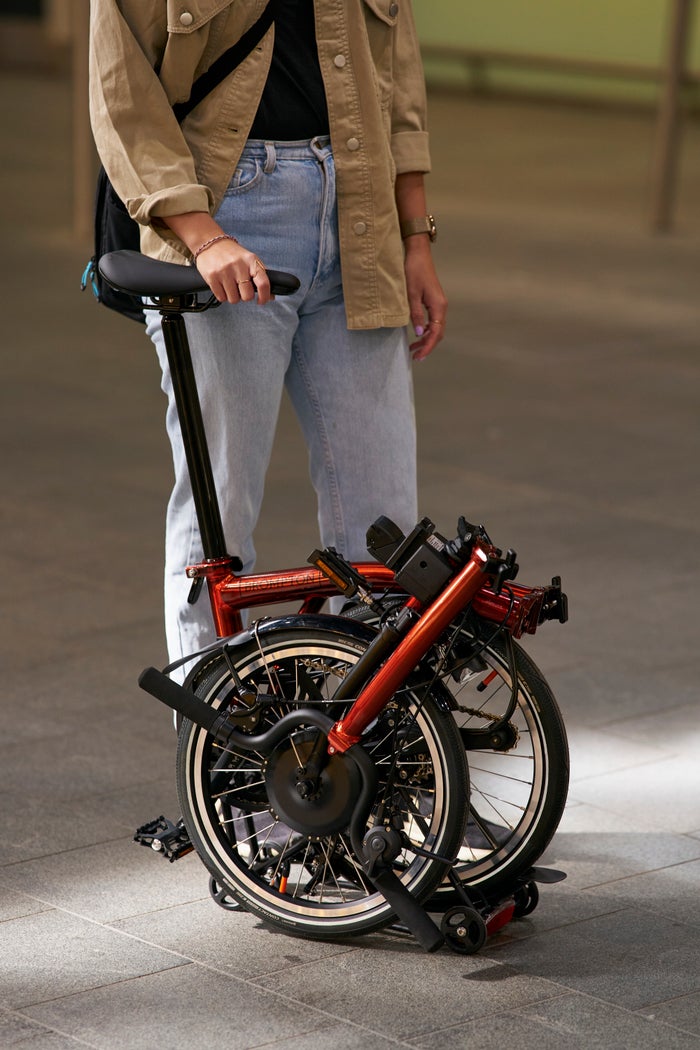 lifestyle image of person stood with a folded electric p line brompton in flame lacquer