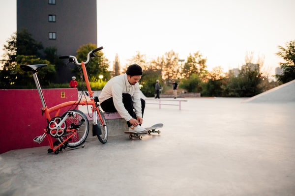 Person tying laces on skateboard next to a folded Brompton
