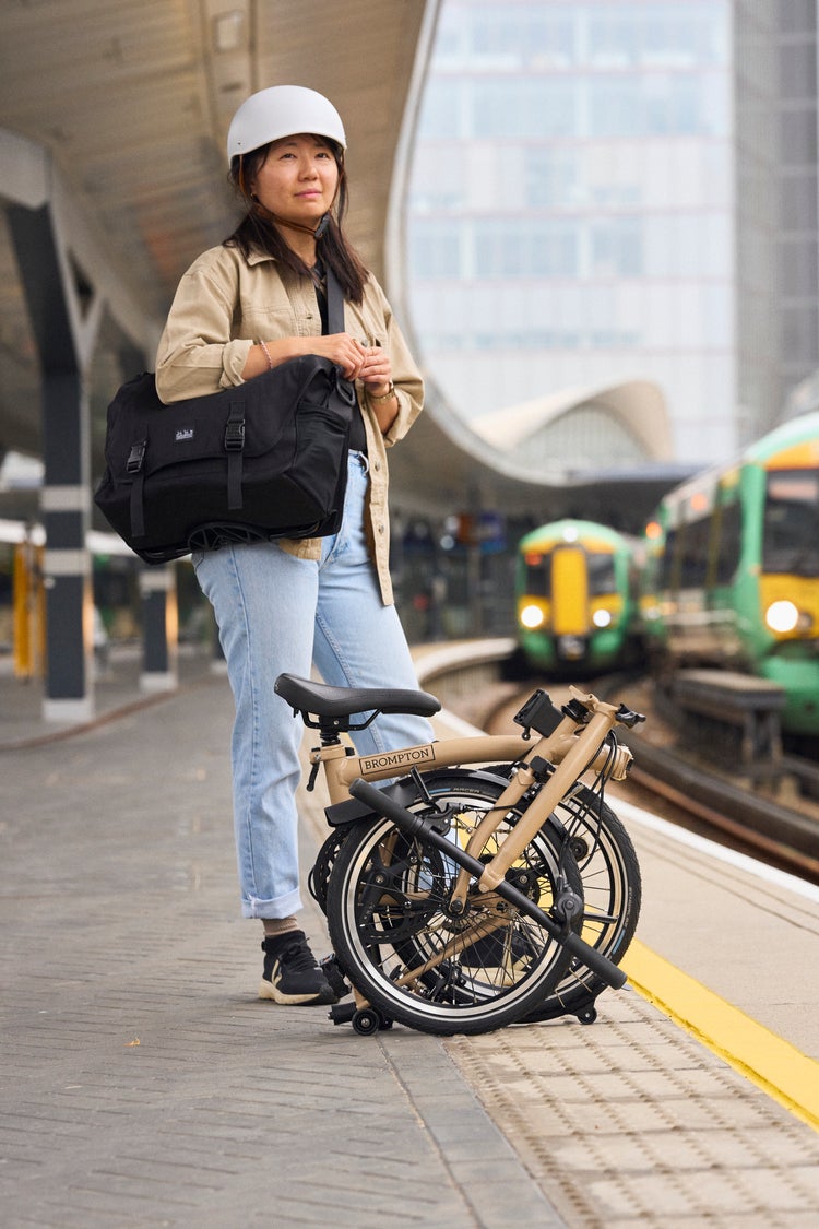 woman stood on train platform with a folded Brompton Electric C Line in Dune Sand 