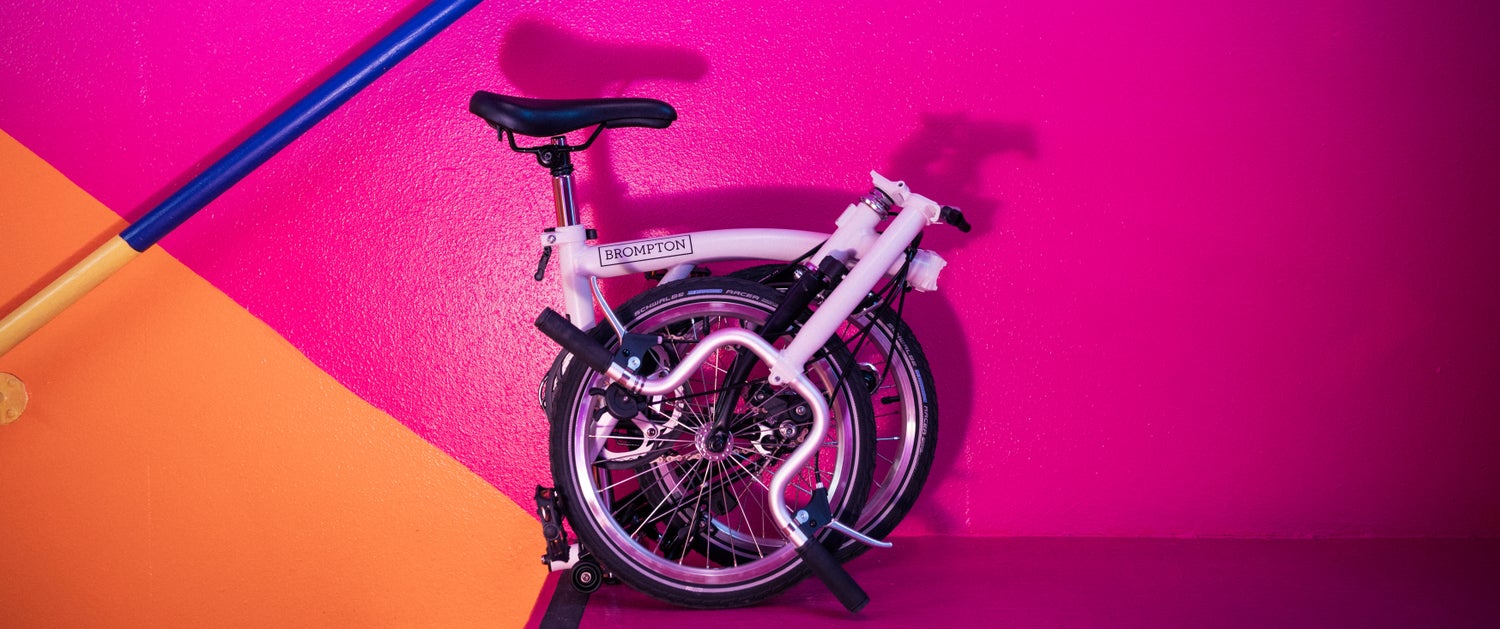 A folded Brompton A Line against a super colorful hot pink and bright orange painted wall