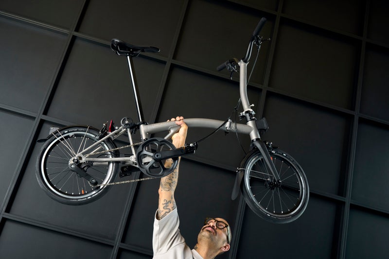 person holding a brompton t line bike above their head