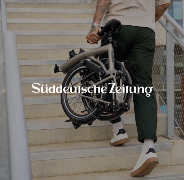 Süddeutsche Zeitung logo over image of person carrying folded Brompton T Line up stairs