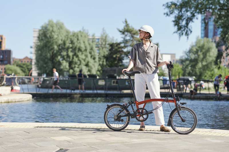 Woman stood with a Flame Lacquer colour Brompton bike