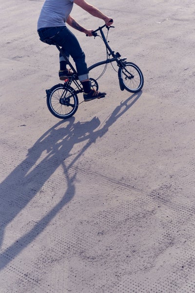 person rolling a folded brompton p line against a yellow backdrop