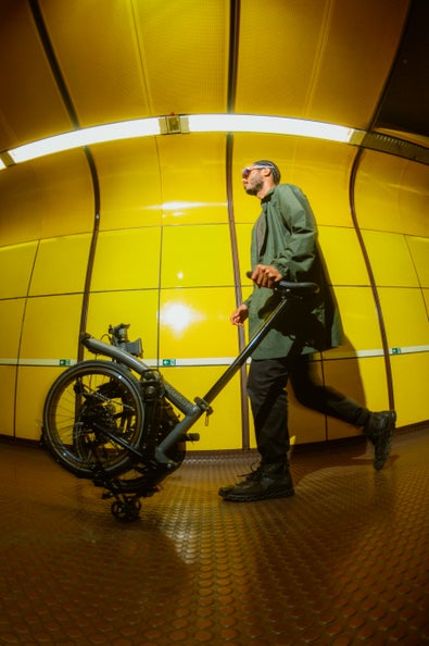 person rolling a folded brompton p line against a yellow backdrop