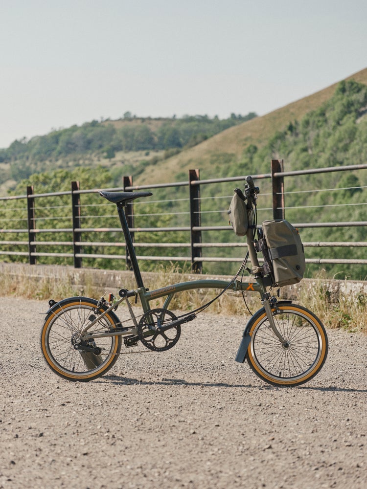 brompton bear grylls collaboration bike lehnt an einem zaun vor einem feld