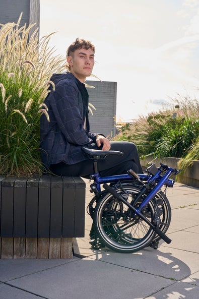 man sitting on a wall with a folded bolt blue brompton p line beside him