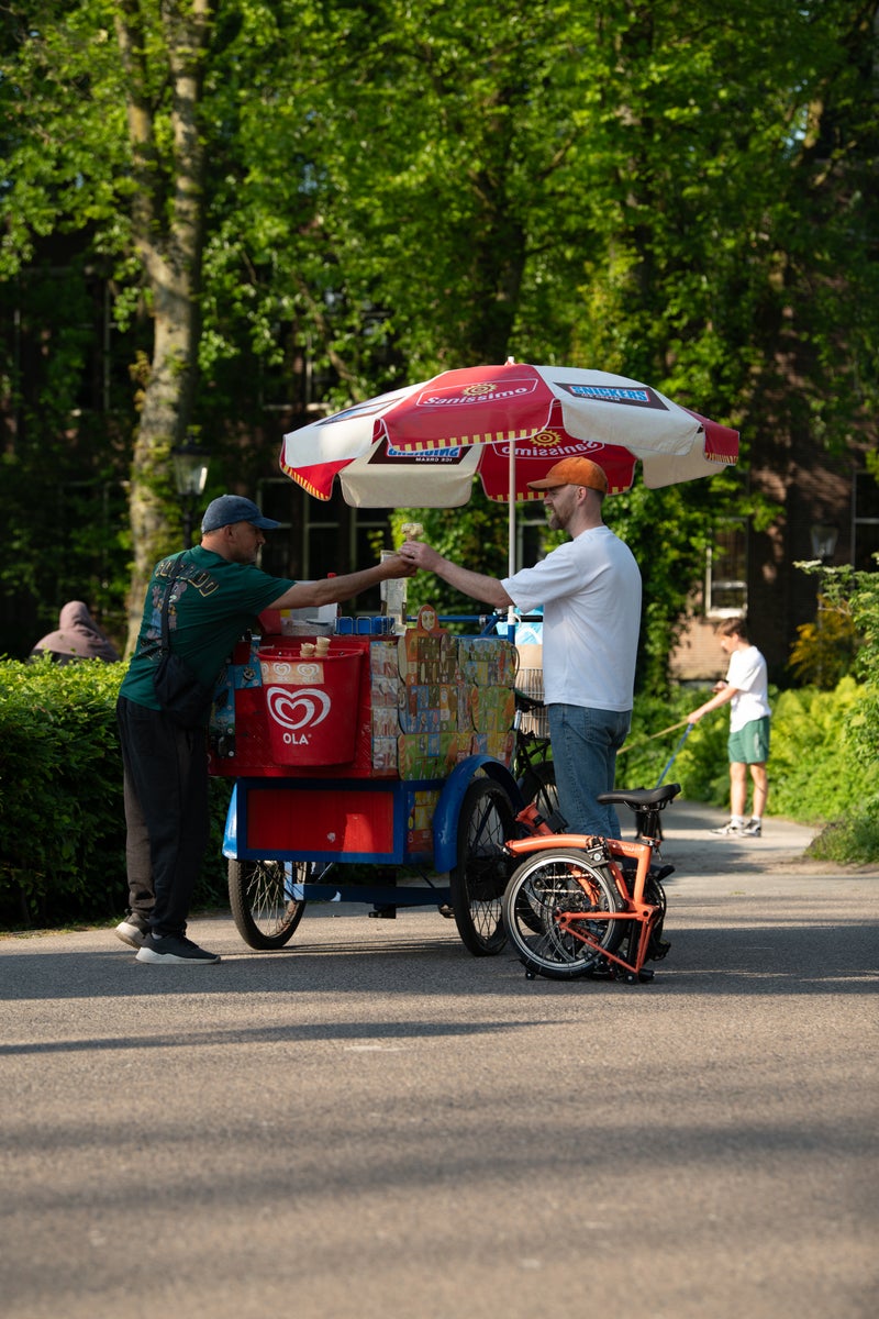 een man koopt een ijsje in amsterdam met een opgevouwen brompton aan zijn zijde