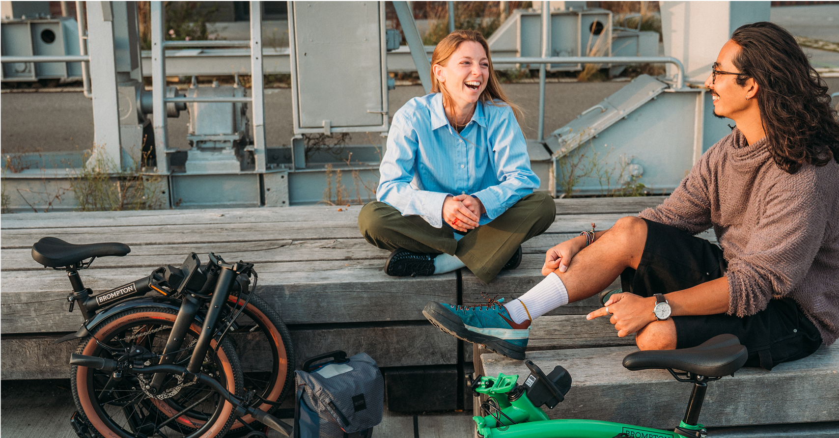 Zwei Leute hängen rum, neben ihnen stehen zwei zusammengeklappte Brompton-Fahrräder.