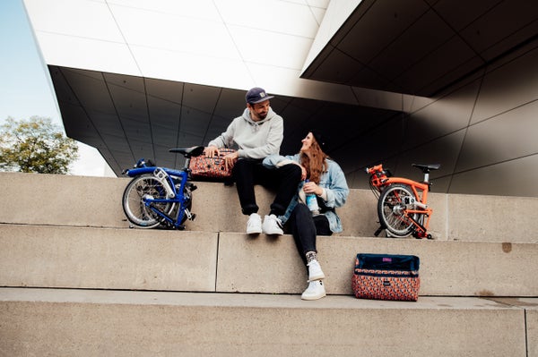 Two people sat on some steps with folded Brompton bikes and luggage