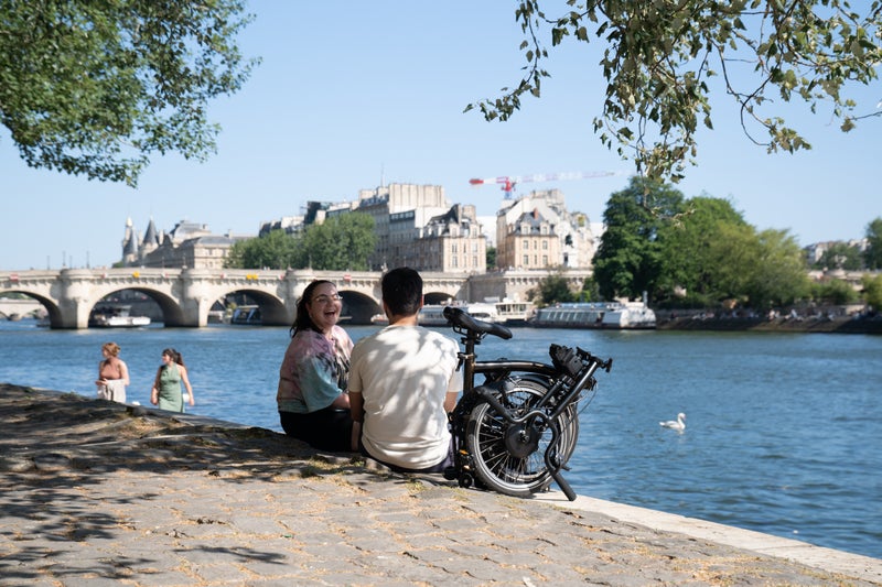 two people sat on riverside in paris with folded brompton bike