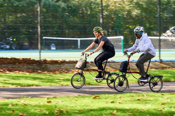 Two women riding Brompton bikes though the park