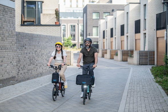 Two people in helmets riding Brompton bikes down a street