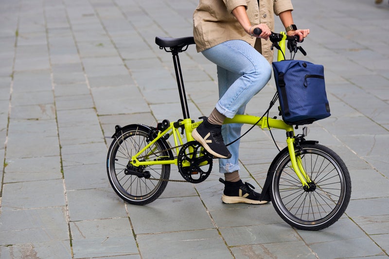 A folded cloud blue Brompton C Line bike being carried into an office