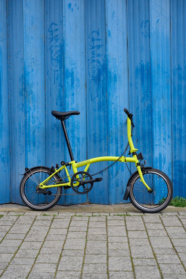 the brompton c line in yuzu lime leaning against blue wall