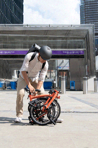 A person folding and unfolding a Brompton C Line in front of the subway