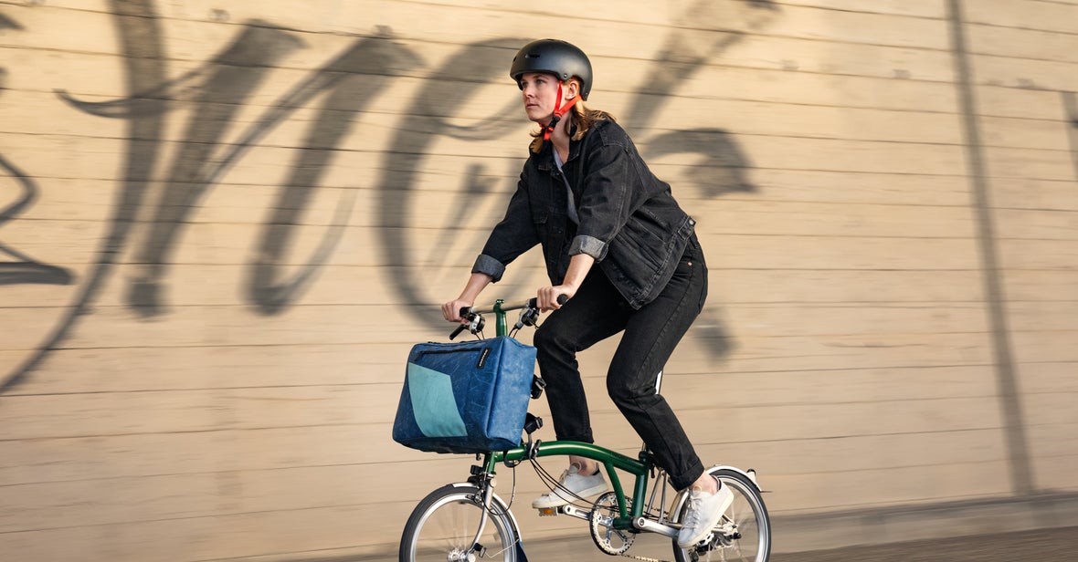 A woman on a Brompton folding bike with a Freitag bag clipped onto the luggage block