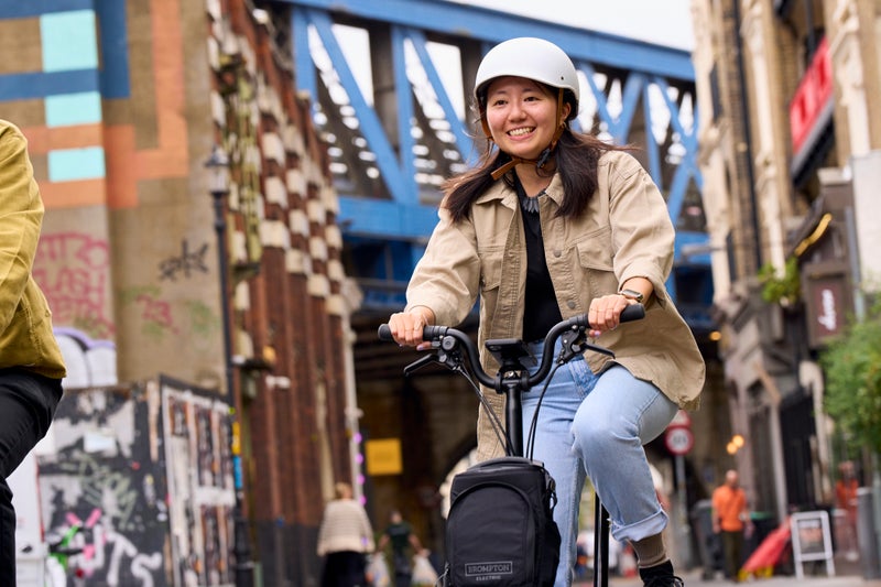 smiling person riding a brompton folding bike through london