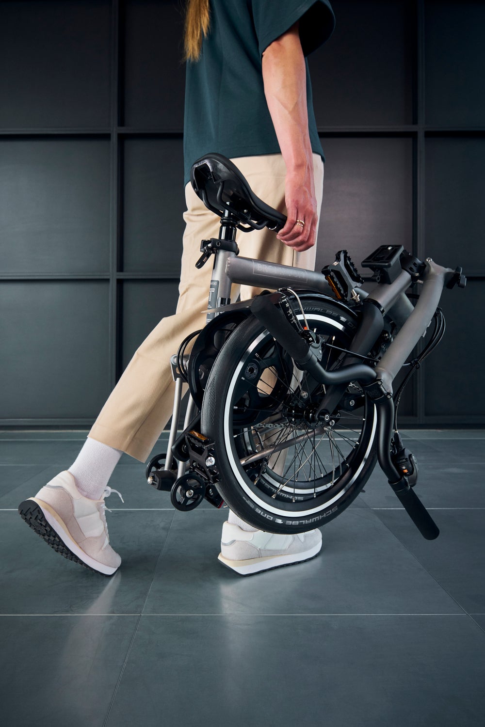 A person carrying a folded Brompton T Line bike in a studio