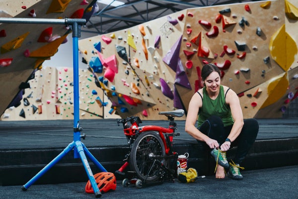 A folded red Brompton with Vanessa in a rock climbing gym