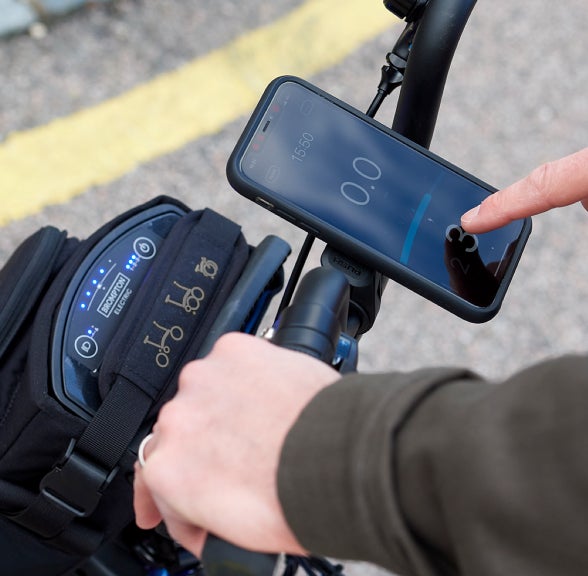 Une image en gros plan d’une personne utilisant l’application Brompton Electric sur son smartphone monté sur le guidon de son vélo