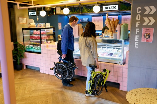 2 people at gelato counter holding their folded brompton c line bikes