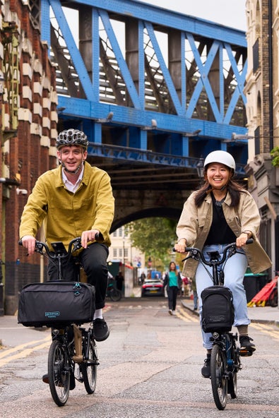 two happy friends riding their Brompton Electric C Lines through the streets of London