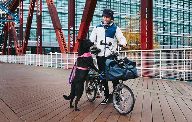 Man op een Brompton-fiets met zijn zwarte hond