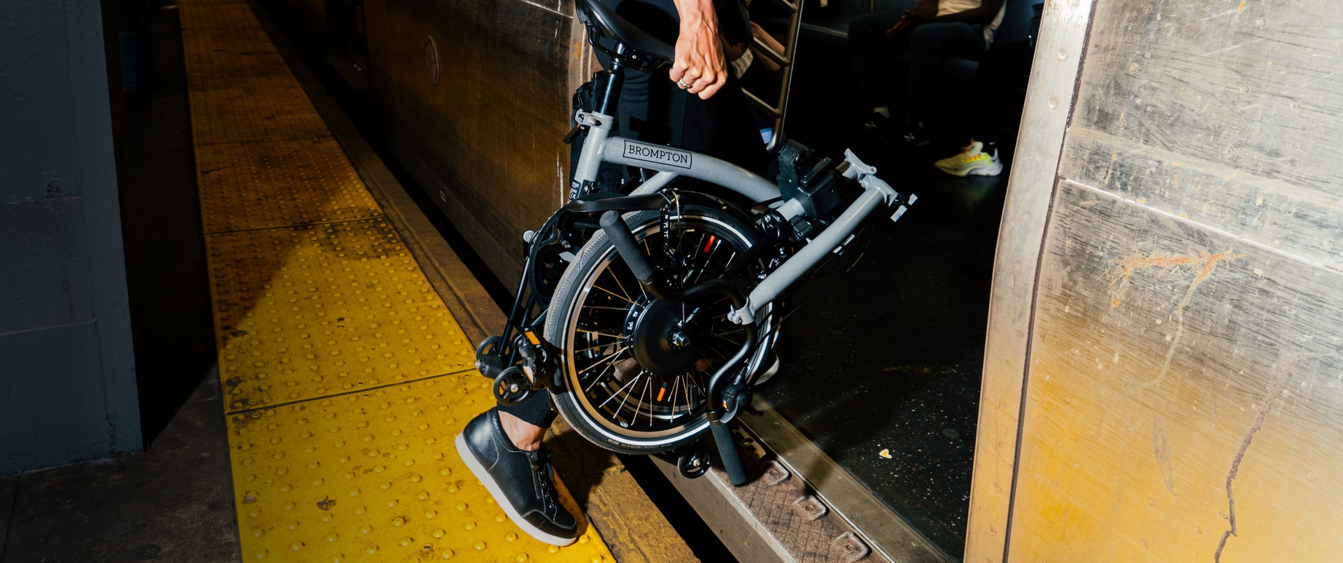 alt="A person carrying a folded Brompton Electric P Line onto the subway"