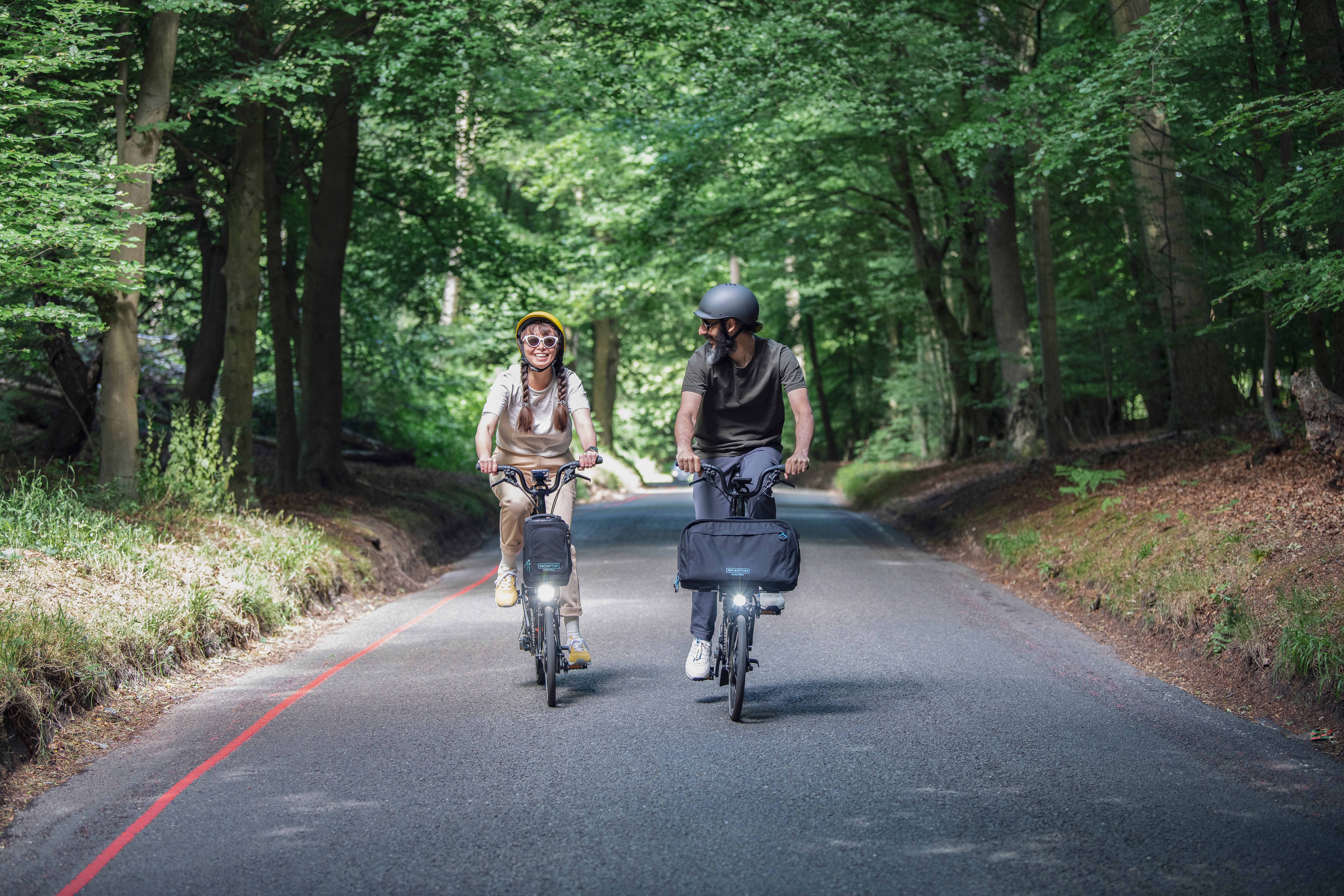 Two happy people riding Brompton Electric C Lines through a woody trail