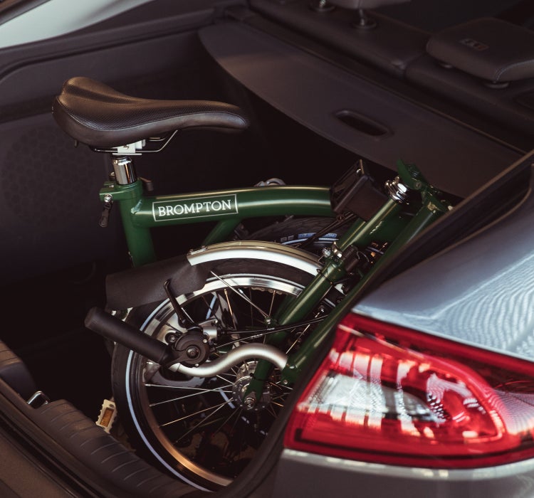 A close-up image of a forest green Brompton C Line folded in the trunk of a car