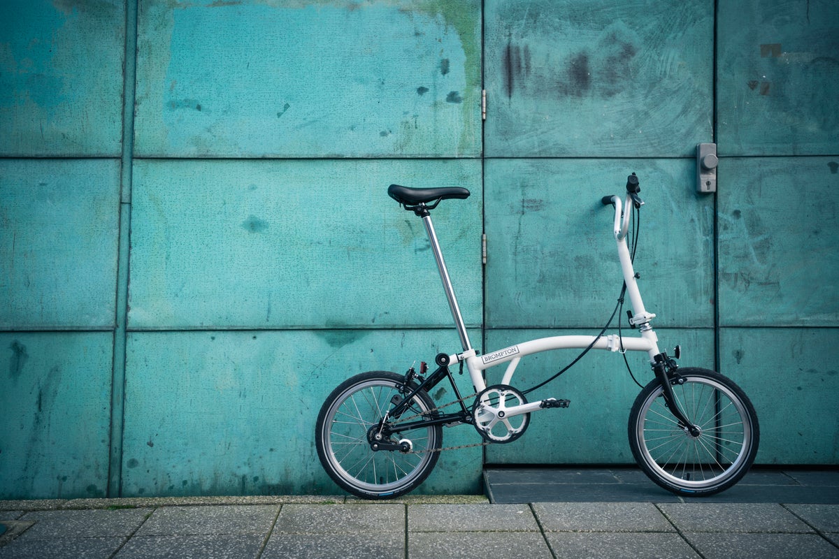 A lifestyle image of a Brompton A Line folding bike leaning against a blue wall