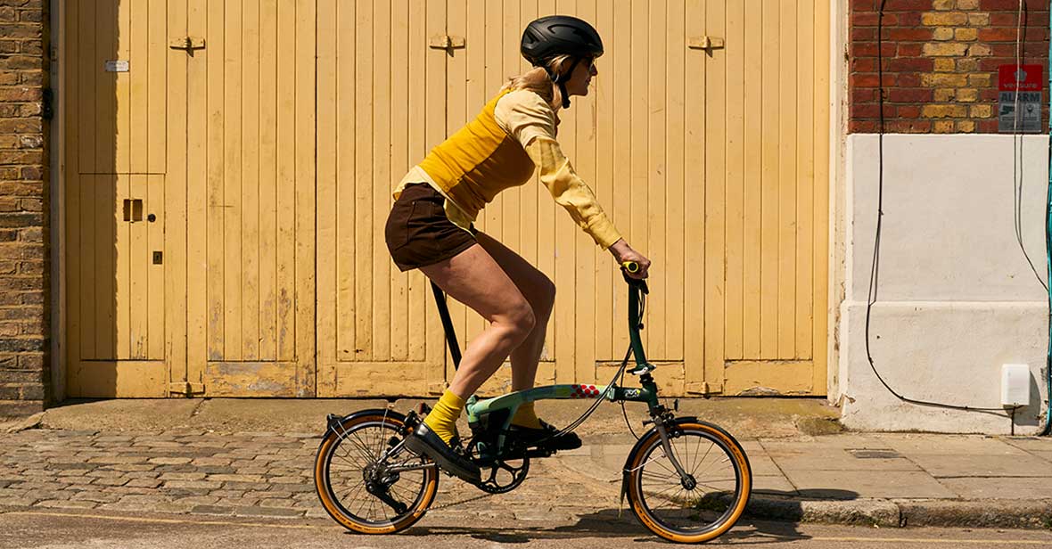 Woman riding Brompton x Tour de France P Line in front of a yellow garage door