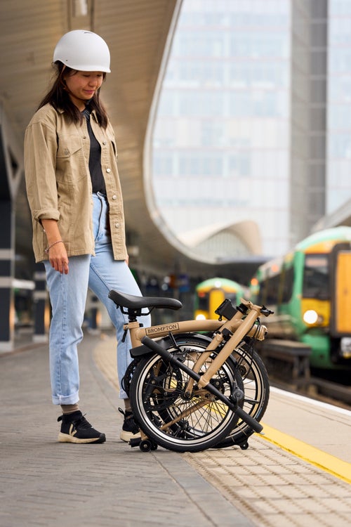 woman stood with her brompton dune sand c line folded on a train platform