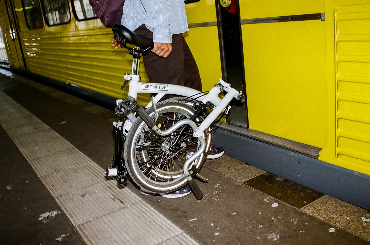 Person, die ein gefaltetes Brompton A Line Fahrrad in den gelben Zug trägt