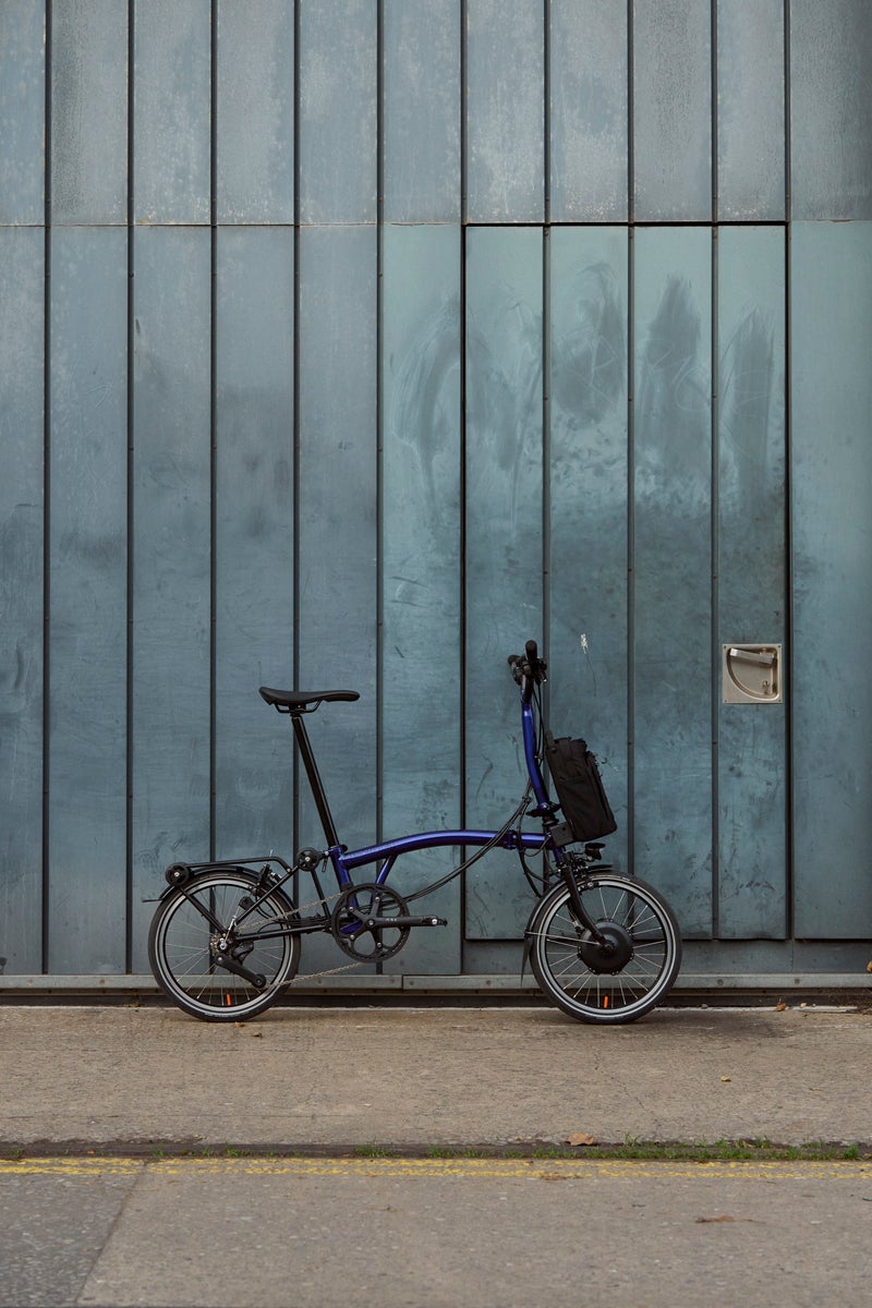 the brompton electric p line 12 speed leaning against blue wall