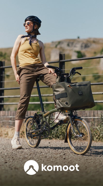 A model on the Brompton x Bear Grylls bike with a white graphic of the Komoot logo