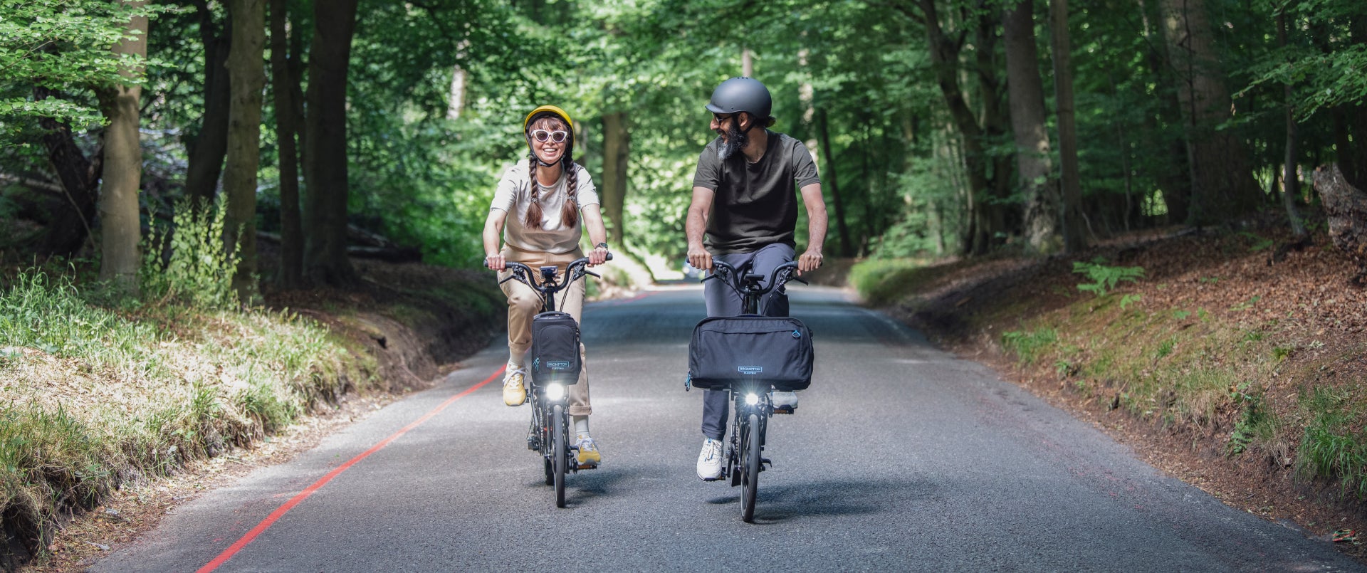 Two happy people riding Brompton Electric C Lines through a woody trail