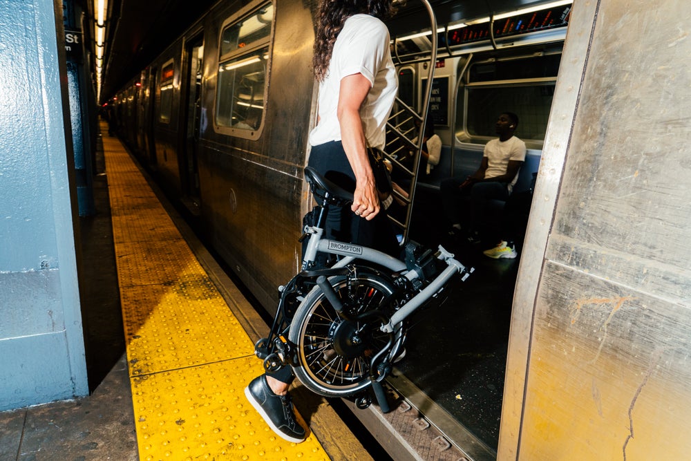 A woman carrying a folded Brompton P Line onto a train